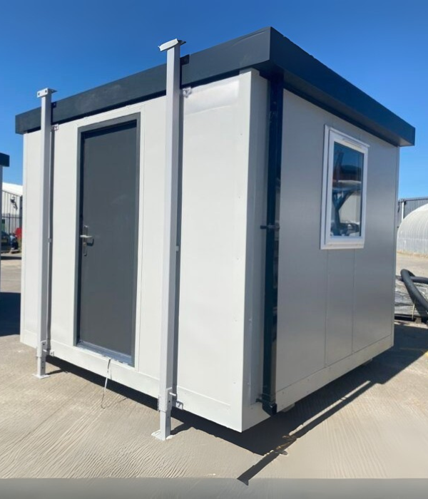 A modern portable office cabin with a gray door and window, set against a clear blue sky.